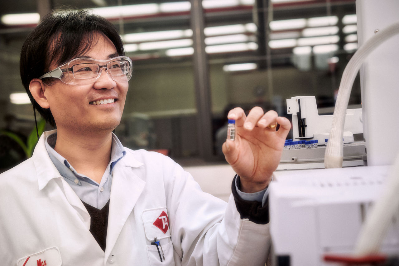 A Teknor Apex Employee in a lab coat with safety glasses handling small tube of chemical for testing