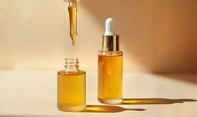 Close-up photo of golden dropper bottles, pipette pouring liquid serum. Golden bottles, serum liquid. Natural light creates shadows. Skincare product shot. Trendy modern beauty product presentation.
