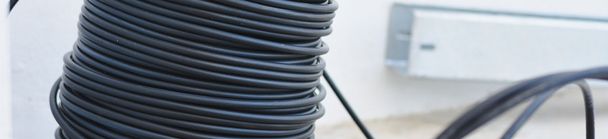 large coil of black cable or wire, neatly wound and placed on the ground. The cable appears to be made of a flexible material, possibly rubber or plastic.