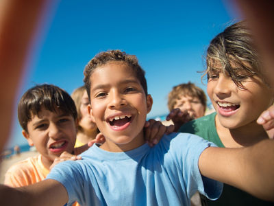 Selfie of cheerful multiethnic preteen boy friends. Portrait of happy kids on beach. Summer vacation and friendship concept