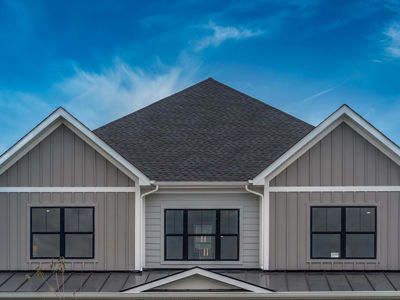 Upscale American house façade with vertical beige vinyl siding white accents, black framed aluminum windows metal roof cover over the porch, double gable roof with dreamy blue sky in the USA