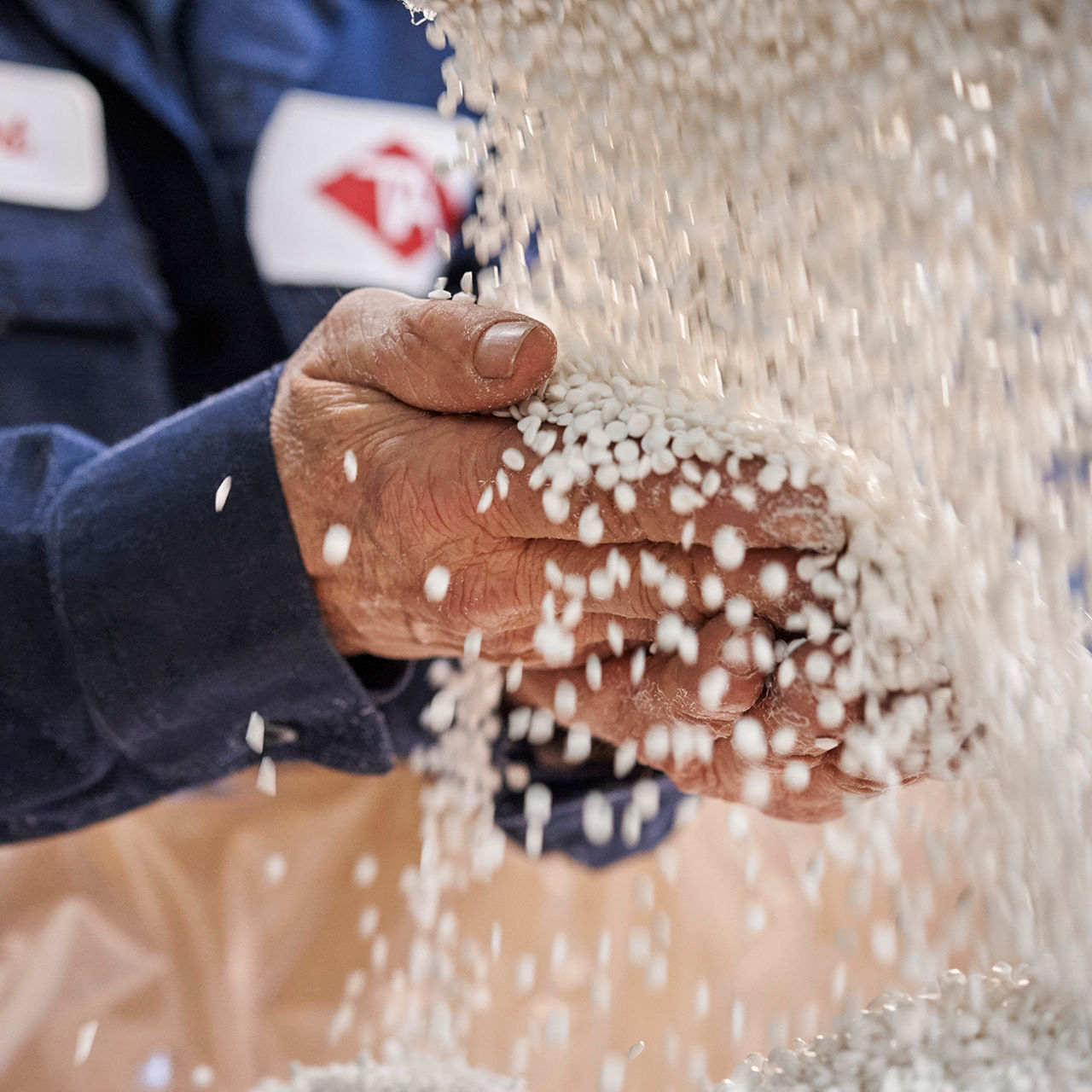 white PVC pellets falling on workers hand in box, worker wearing a blue overall with TA sign stiched