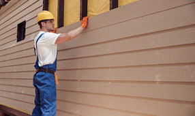Handsome young man construction worker wearing safety helmet and work overalls while installing wood siding