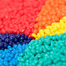 Colorful arrangement of polymer pellets, in red, orange, yellow, green, light blue and indigo