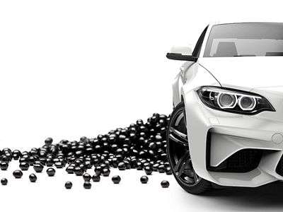 Black shiny polymer pellets are laid on white background, in front of it, a white sports car is placed 