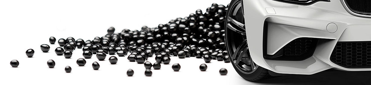 Black shiny polymer pellets are laid on white background, in front of it, a white sports car is placed 
