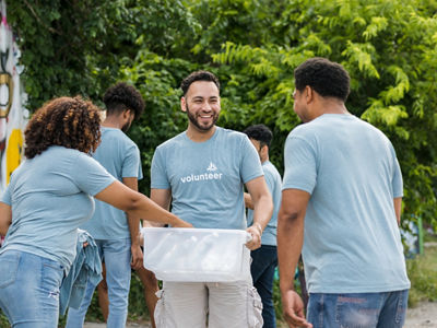 The young adult male volunteer stands near his friends to pass out painting supplies.